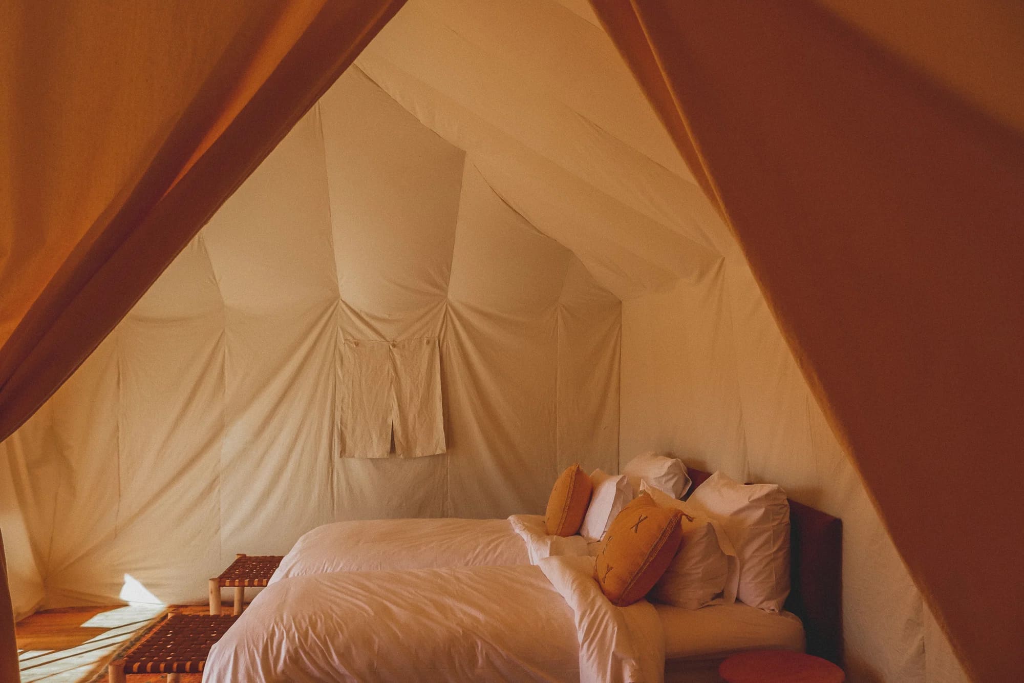 Bett mit weißer Bettwäsche und ockerfarbenen Kissen im Zelt